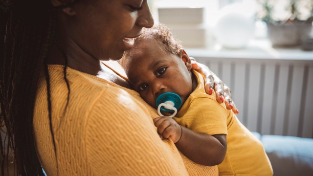 A mother snuggling her newborn who is sucking on a pacifier despite one of the baby myths that pacifiers cause nipple confusion